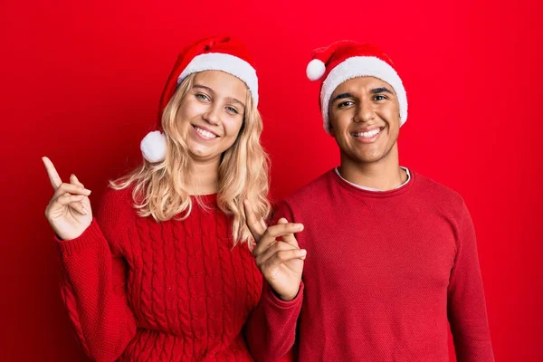 Young Interracial Couple Wearing Christmas Hat Smiling Happy Pointing Hand — Stock Photo, Image