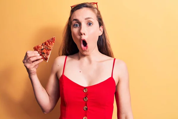 若いです美しいですブロンド女性食べるピザのスライスを身に着けている夏のドレス怖がってと驚きのために口を開けて驚いて 不信顔 — ストック写真