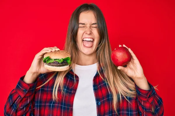 Piękna Biała Kobieta Porównując Hamburgera Zdrowe Czerwone Jabłko Wystający Język — Zdjęcie stockowe