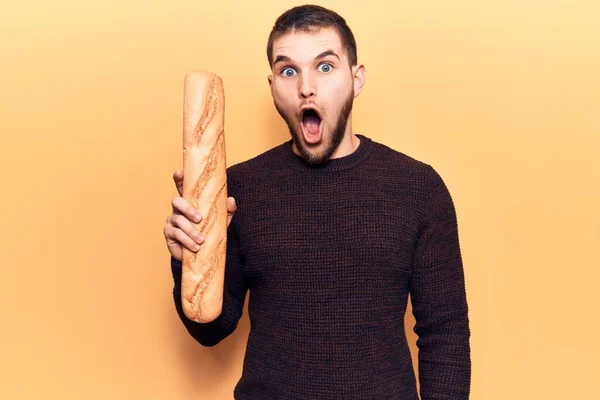 Young Handsome Man Holding Baguette Scared Amazed Open Mouth Surprise — Stock Photo, Image