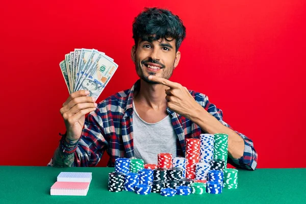 Jovem Hispânico Sentado Mesa Com Fichas Poker Cartas Segurando Dólares — Fotografia de Stock