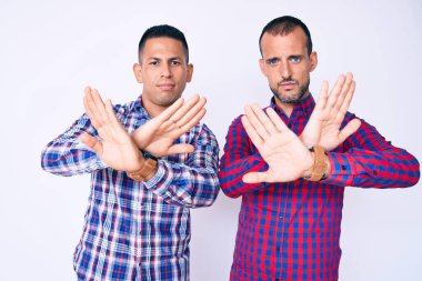 Gündelik kıyafetler giyen iki genç eşcinsel. Reddedilmiş yüz ifadesi. Kollarını kavuşturup negatif işaret veriyor. 