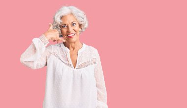 Yaşlı, gri saçlı, günlük kıyafetler giyen, gülümseyen, el ve parmaklarıyla telefonla konuşan bir kadın. iletişim kavramları. 