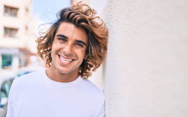 Genç yakışıklı İspanyol gülümseyen mutlu bir adam şehrin duvarına yaslanıyor.