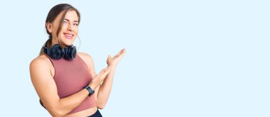 Güzel beyaz kadın spor kıyafetleri giyip kulaklık takıyor ve gülümseyerek içeri giriyor. 