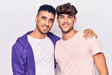 Genç eşcinsel çift yüzüne mutlu ve havalı bir gülümsemeyle gökkuşağı lgtbq bayrağı çiziyor. şanslı kişi. 