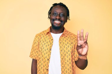 Saçları örgülü genç Afro-Amerikan bir adam üç numarayı gösterip gösterirken kendinden emin ve mutlu bir şekilde gülümsüyor.. 