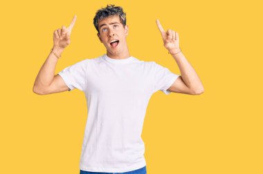 Gündelik beyaz tişört giyen genç yakışıklı adam şaşırmış, şaşırmış, parmaklarıyla işaret ediyor ve kollarını kaldırıyordu.. 