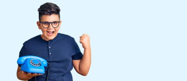 Küçük çocuk telefonda gururla bağırıyor, zaferi kutluyor ve kollarını kaldırarak heyecanlanıyor. 