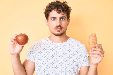 Kıvırcık saçlı, elma ve kruvasan tutan genç beyaz adam yüzünde ciddi bir ifadeyle rahatlamış. Basit ve doğal bir şekilde kameraya bakıyorsun.. 