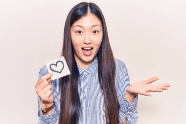 Genç, güzel Çinli bir kadın kalp şeklinde hatırlatıcı tutuyor başarıyı mutlu bir gülümsemeyle kutluyor ve kazanan el kaldırarak ifade ediyor. 