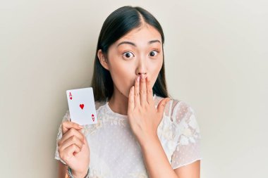 Genç Çinli bir kadın elinde as poker kartı tutarak ağzını eliyle kapatmış, şok olmuş ve hata yapmaktan korkan. şaşırmış ifade 