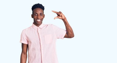 Gündelik kıyafetler giyen, gülümseyen, kendine güvenen, el hareketi yapan, parmaklarıyla işaret yapan ve kameraya bakan genç Afro-Amerikan bir adam. ölçüm kavramı. 