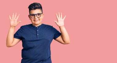 Gündelik kıyafetler giyen ve gözlük takan küçük çocuk 10 numarayı gösterip işaret ederken kendinden emin ve mutlu bir şekilde gülümsüyor.. 