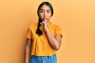 Gündelik giysiler giyen genç Latin kadın parmakları dudaklarında sessiz olmak istiyor. sessizlik ve gizli konsept. 