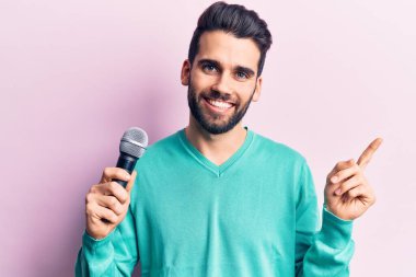 Sakallı genç yakışıklı adam mikrofon kullanarak şarkı söylüyor. Gülümsüyor, mutlu bir şekilde işaret ediyor. 