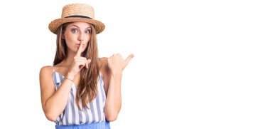 Yaz şapkası takan genç ve güzel sarışın kadın sessiz olmak istiyor. Parmakları dudaklarında, elleri yanda. sessizlik ve gizli konsept. 