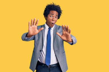Afro saçlı, iş ceketi giyen yakışıklı Afro-Amerikalı. El hareketlerini, kızgın ve hayal kırıklığına uğramış yüz ifadesiyle durduruyor. 