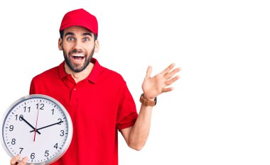 Sakallı yakışıklı adam büyük bir saat tutuyor zaferi kutluyor mutlu bir gülümsemeyle ve ellerini kaldırarak kazanan bir ifadeyle. 