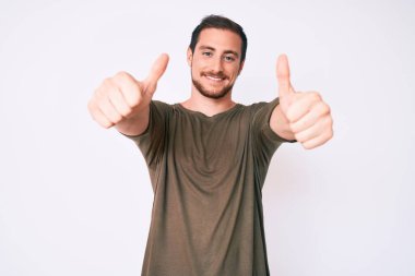 Gündelik giysiler giyen genç bir adam elinle olumlu jest yapıyor, gülümsüyor ve başarı için seviniyor. kazanan jest. 