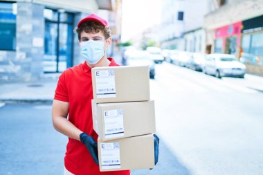 Coronavirus koruması takan beyaz bir kurye elinde karton paketler, şehirde yürüyor..