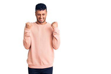 Gündelik kıyafetler giyen genç İspanyol adam başarı için heyecanlı kolları havada ve gözleri kapalı zaferi kutlarken gülümsüyor. Kazanan konsept. 