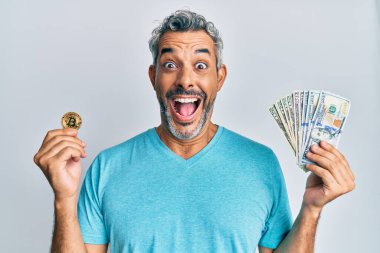 Orta yaşlı, kır saçlı, elinde dolar, bitcoin tutan bir adam çılgınlığı kutluyor ve başarıya hayret içinde bakıyor, heyecanla haykırıyor.. 