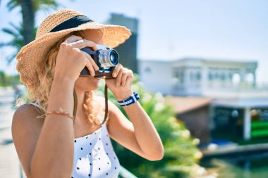 Sarışın, güzel, beyaz bir kadın. Bir yaz günü açık havada mutlu bir şekilde gülümsüyor. Klasik kamera kullanıyor.