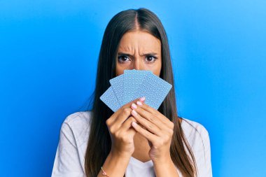 Kumarda poker oynayan genç İspanyol kadın kartlarla yüzünü kapatıyor şüpheci ve gergin, sorun yüzünden suratını asıyor. negatif kişi. 
