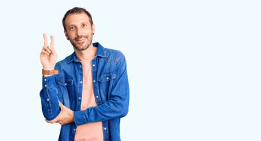 Sıradan kıyafetler giyen, gülen, kameraya göz kırpan, zafer işareti yapan genç yakışıklı bir adam. İki numara.. 