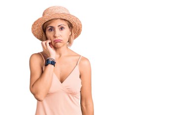 Sarışın, yaz şapkası takan genç bir kadın yorgun ve bunalımdan sıkılmış görünüyor.. 