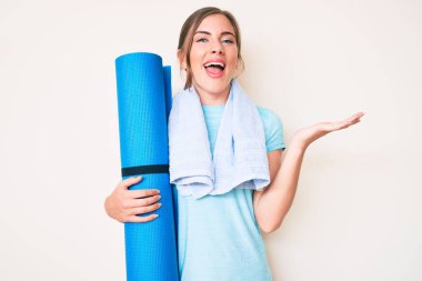 Güzel beyaz kadın yoga minderini tutarak zaferi mutlu bir gülümsemeyle kutluyor ve kazanan el kaldırarak ifade ediyor. 