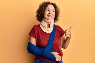 Güzel, orta yaşlı, boyun tasması ve kol takan olgun bir kadın başparmağını yana uzatıyor ve ağzı açık gülümsüyor. 