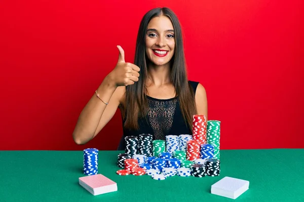 Jovem Hispânica Sentada Mesa Jogando Poker Sorrindo Feliz Positivo Polegar — Fotografia de Stock