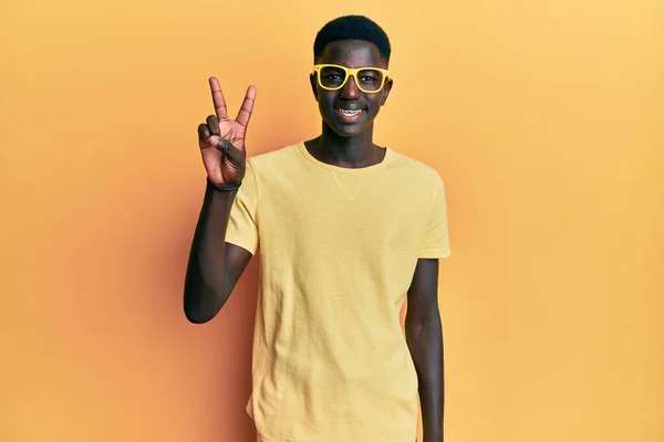 自信と幸せ笑顔ながら カジュアルな服と眼鏡を身に着けている若いアフリカ系アメリカ人の男性は 指の数2を示すと指摘 — ストック写真