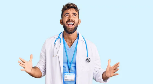 医師の制服を着た若いヒスパニック系の男と狂った叫びと積極的な表現と腕を上げて叫んで聴診器 フラストレーションコンセプト — ストック写真