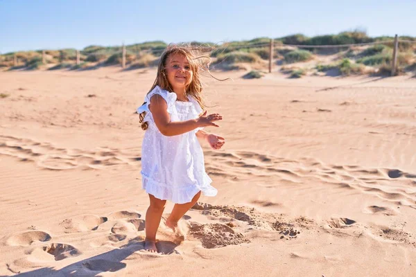 幸せなブロンドの子供は夏のドレスを着て笑顔 ビーチで砂の上で遊んで顔に笑顔で立って — ストック写真