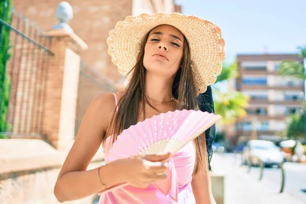 Tatilde olan genç İspanyol kadın yaz stili giyiniyor. Şehrin sokaklarında el yelpazesi kullanıyor.