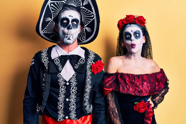 狂気とコミカルなジェスチャーで魚の顔を作る黄色の上に死んだ衣装のメキシコの日を身に着けている若いカップル 面白い表現 — ストック写真