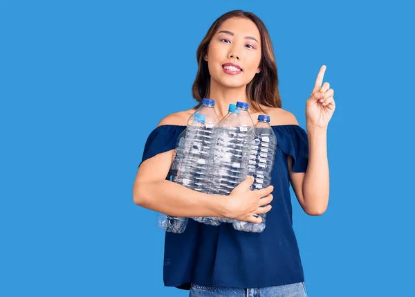 年轻美丽的中国女孩拿着回收的塑料瓶 满脸喜形于色 惊讶地提出了一个主意或问题 — 图库照片