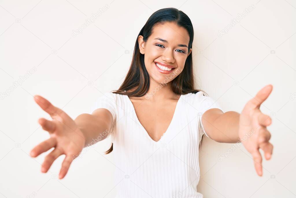 Young beautiful latin girl wearing casual white tshirt looking at the camera smiling with open arms for hug. cheerful expression embracing happiness. 