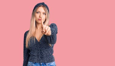 Genç, güzel, sarışın, gündelik giysiler giymiş, parmağını kaldırmış, kızgın bir ifade takınan, hiçbir hareket göstermeyen bir kadın. 