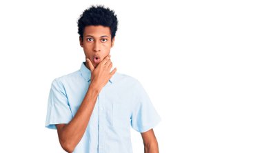 Gündelik giysiler giyen genç Afro-Amerikan erkeği elleri çenesinde olan inançsızlıktan, şaşkınlıktan ve şaşkınlıktan büyülenmiş görünüyor. 