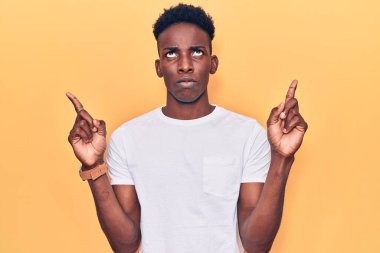 Genç Afro-Amerikan adam günlük giysiler giymiş üzgün ve üzgün görünüyor, parmaklarıyla yön gösteriyor, mutsuz ve depresif.. 