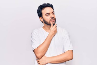 Elleri çenesinde gündelik giysiler içinde soru soran genç İspanyol bir adam, düşünceli bir ifade. Düşünceli bir yüzle gülümsüyor. şüphe kavramı. 