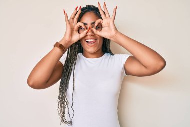 Örgülü beyaz tişörtlü Afro-Amerikalı genç bir kadın dürbün gibi güzel hareketler yapıyor, gözleri parmaklarından bakıyor. çılgın ifade. 