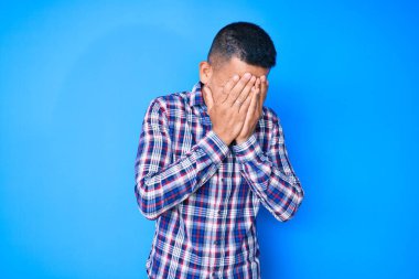 Genç, yakışıklı, gündelik kıyafetler giyen, suratını ellerle örten ve ağlayan Latin bir adam. depresyon kavramı. 
