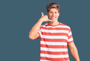 Genç, yakışıklı, sıradan kıyafetler giymiş, gülümseyen, el ve parmaklarıyla telefonla konuşan bir adam. iletişim kavramları. 