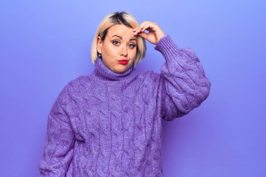 Güzel sarışın ve cüsseli bir kadın mor arka plan üzerine balıkçı yaka kazak giyiyor. Alnındaki sorun yüzünden endişeli ve stresli. Kriz için endişeli.
