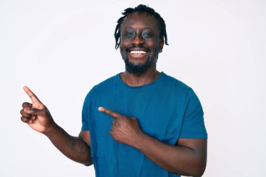 Saçları örgülü, gülümseyen ve kameraya bakıp iki eliyle ve parmaklarıyla yüzünü gösteren Afro-Amerikan genç adam.. 